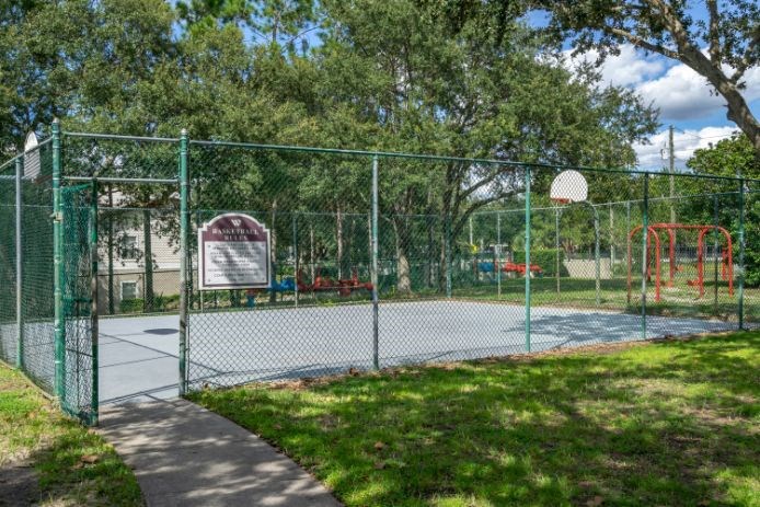 Outdoor basketball court surrounded by native landscaping and playground in the background