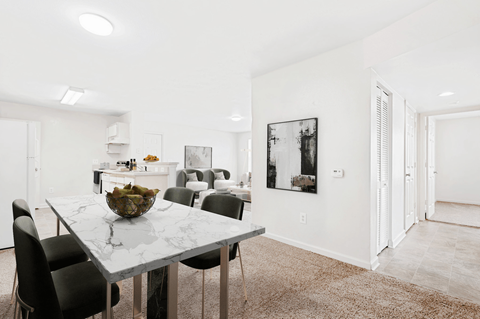 Virtually staged dining room with marble table and green accent chairs. Kitchen and living room in background