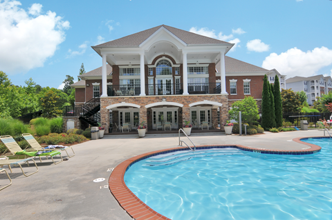 Community pool with pool furniture throughout. The clubhouse is in the background, surrounded by trees.