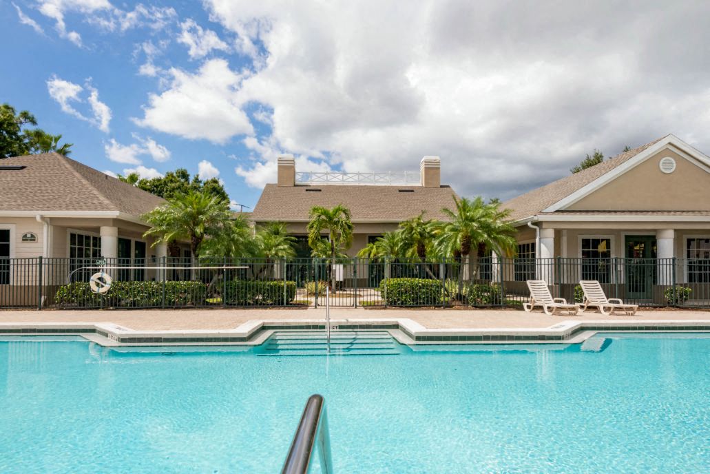Leasing Office Exterior with Swimming Pool and Sun Deck with Lounge Chairs with Trees and Building Exteriors in the Background