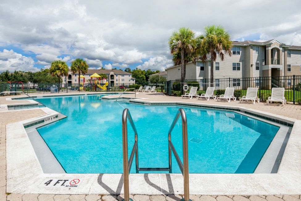 Swimming Pool and Sun Deck with Lounge Chairs with Trees and Building Exteriors in the Background