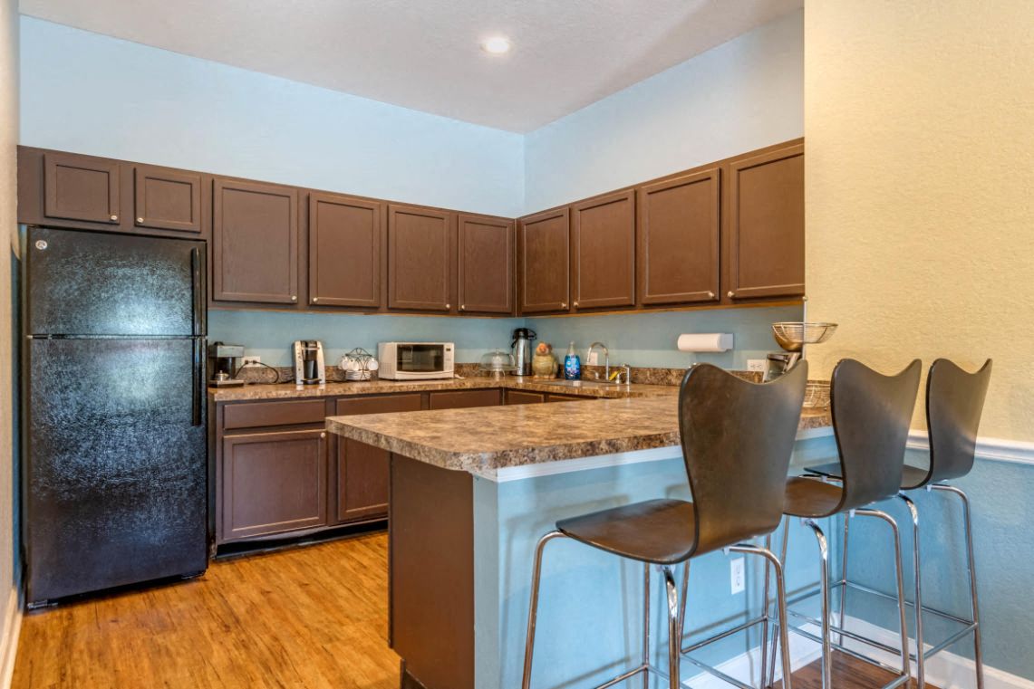 A kitchen with brown chairs and a black fridge.