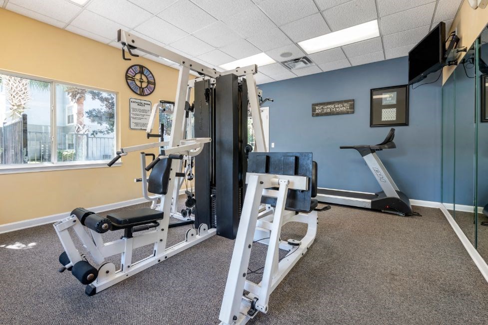 Fitness center strength training equipment, cardio equipment, wall mounted television, wall mirrors, and window for natural lighting