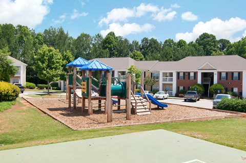 A playground with a blue canopy and a slide is surrounded by houses.