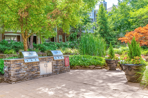 a brick patio with a barbecue and trees in the background at Elan at Mallard Creek Apartment Homes, North Carolina, 28269