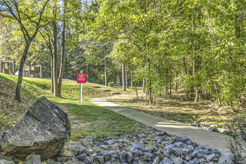a path through a park with a red sign in the background at Elan at Mallard Creek Apartment Homes, Charlotte, NC