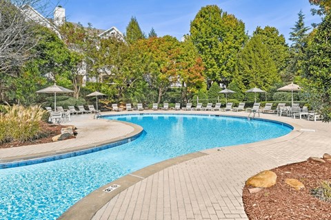 A large outdoor swimming pool surrounded by trees and chairs.