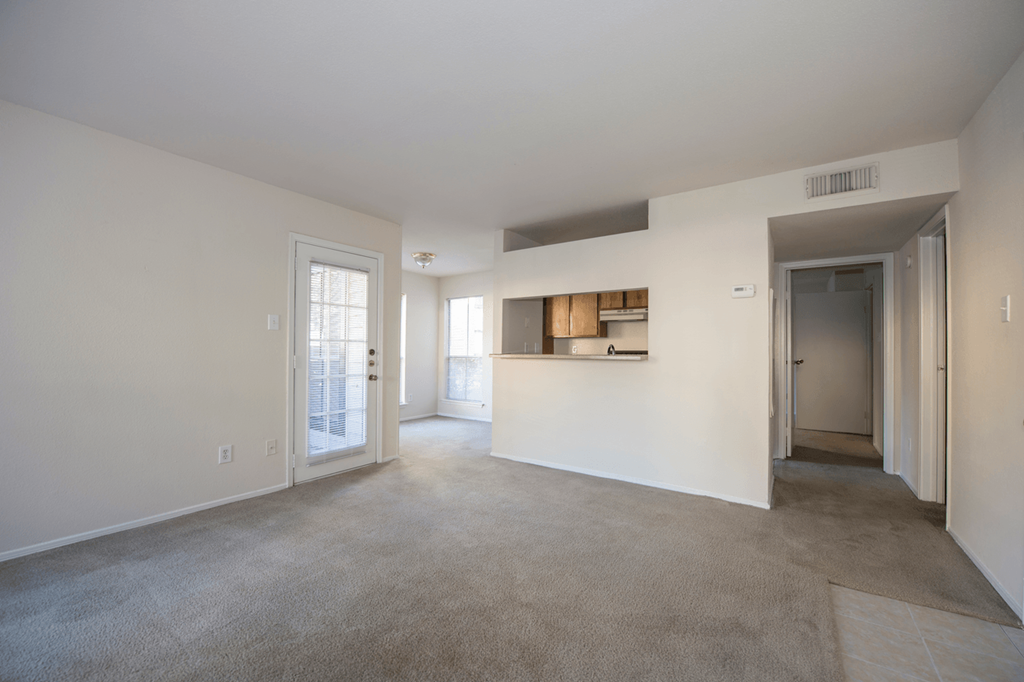 the living room and kitchen of an apartment with white walls and carpet