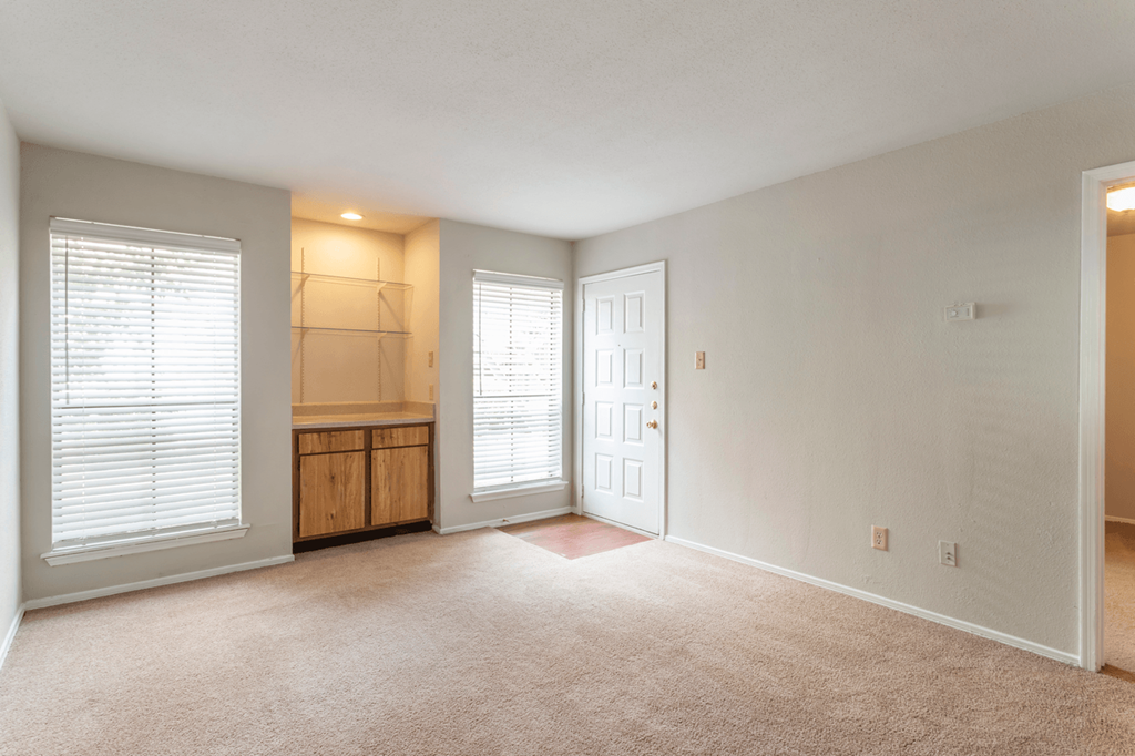 an empty living room with a door to a kitchen