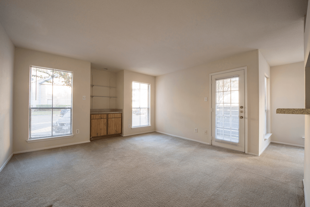 an empty living room with a door to a kitchen