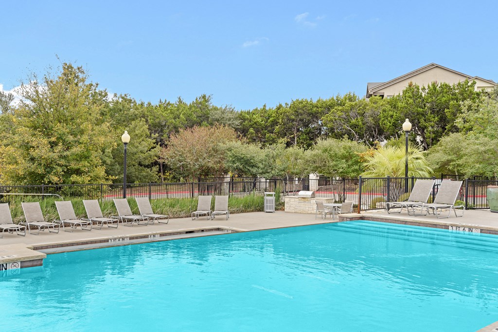 a swimming pool with chaise lounge chairs and trees in the background