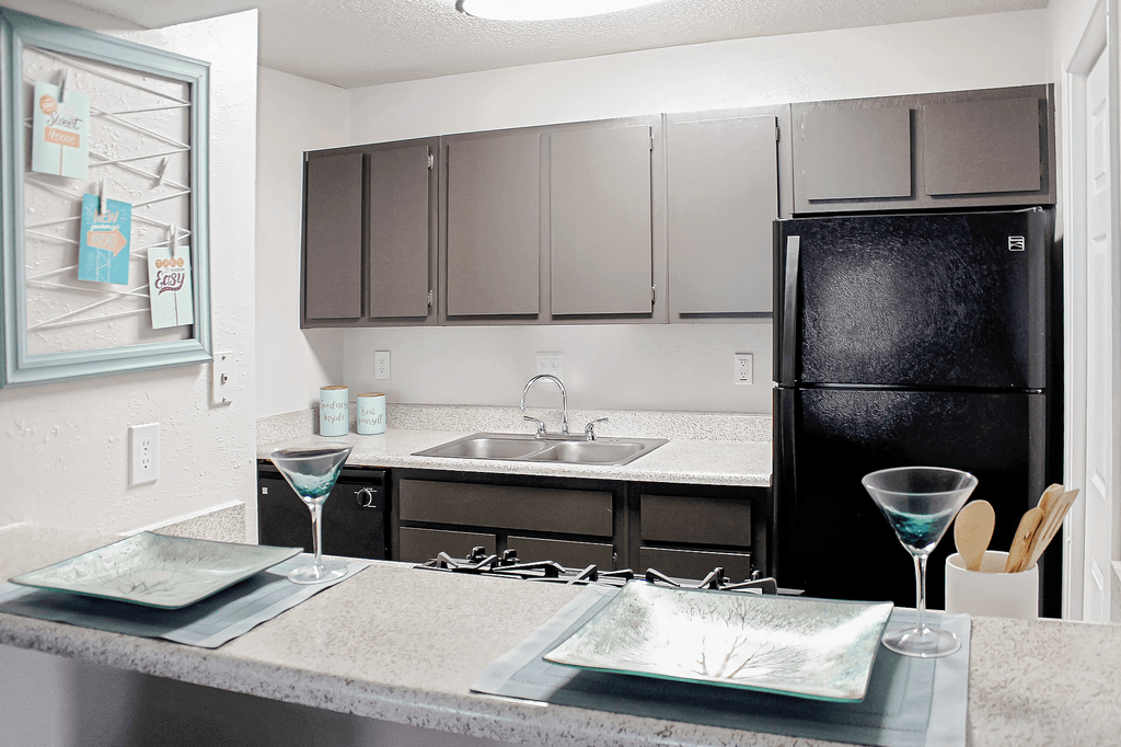 a kitchen with a black refrigerator and sink and a counter with glasses