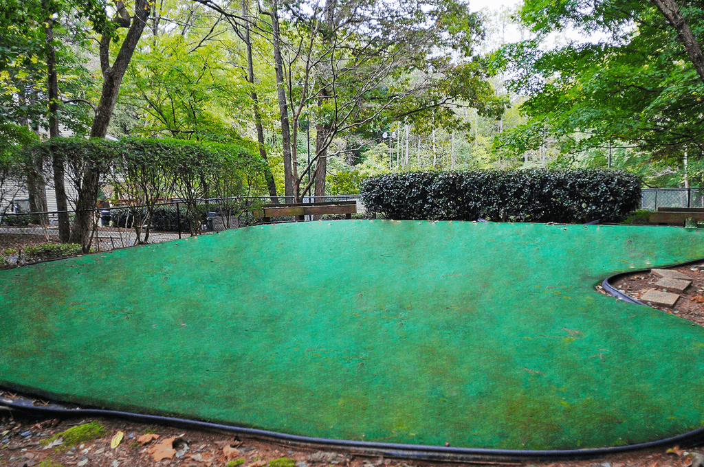 a large green trampoline in a park with trees
