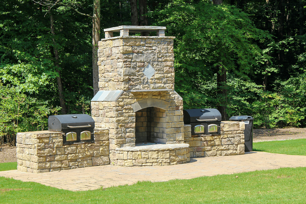 an outdoor stone fireplace with a grill in a park