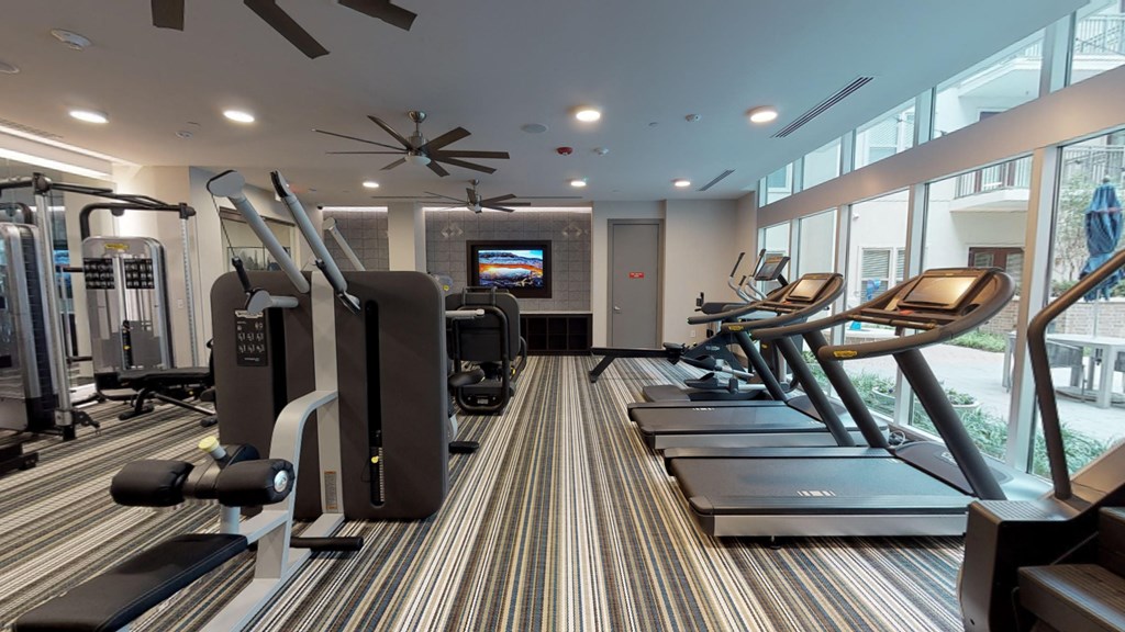 Interior of fitness center facing treadmills, workout equipment, and exterior windows