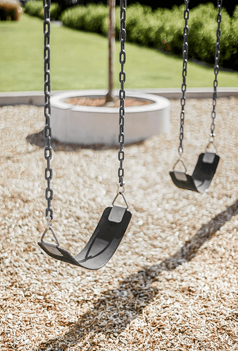 Two empty swings hanging from chains in a playground.