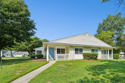 A house with a blue door and white trim is surrounded by green grass and trees.