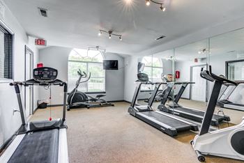 The Fitness Center has carpet throughout, one wall of mirrors, a large picture window with blinds, and a mounted television in the corner. It is equipped with two treadmills, an elliptical and a stationary bicycle.