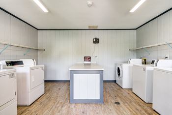 The Laundry Center has white walls and hardwood style flooring. It is equipped with multiple washers and dryers.