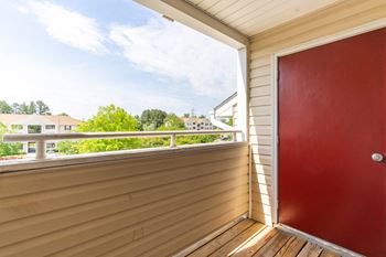Private balcony with a red storage door and a view of the trees in the background