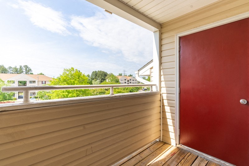 Balcony view with red storage door and view of trees in the background