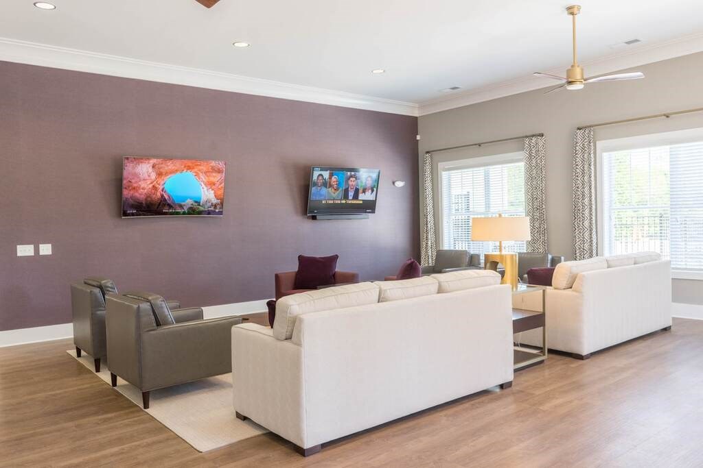 A living room with a white couch, grey armchairs, and a television on the wall at Foxwood Apartments, Raleigh-Durham, NC, 27616