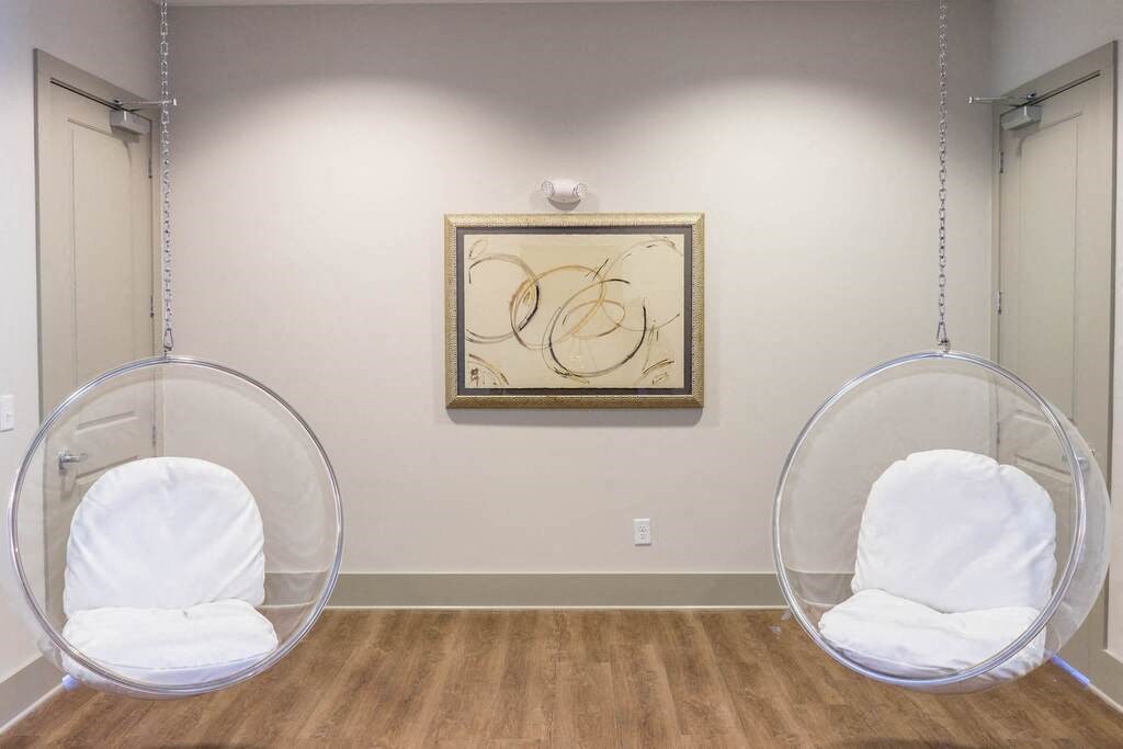Two white chairs are suspended from the ceiling in a room with a framed artwork on the wall at Foxwood Apartments, North Carolina