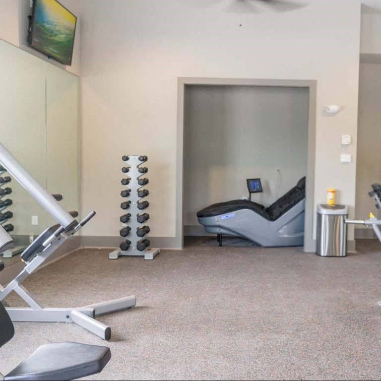 A gym room with a treadmill, weights, and a chair at Foxwood Apartments, Raleigh-Durham