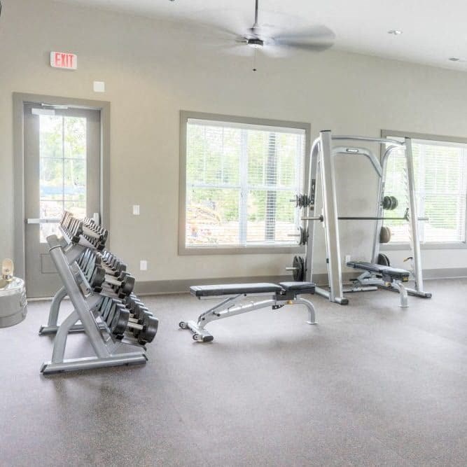 A gym with a row of dumbbells, a bench, and a weight machine at Foxwood Apartments, Raleigh-Durham, NC