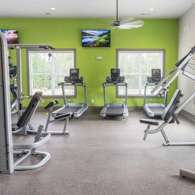 A gym with treadmills, elliptical machines, and a television at Foxwood Apartments, North Carolina