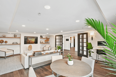 A modern living room with a white sofa set, a wooden coffee table, and a large painting on the wall.