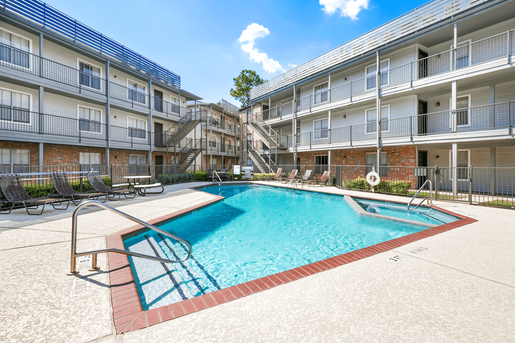 a swimming pool with chaise lounge chairs and an apartment building in the background