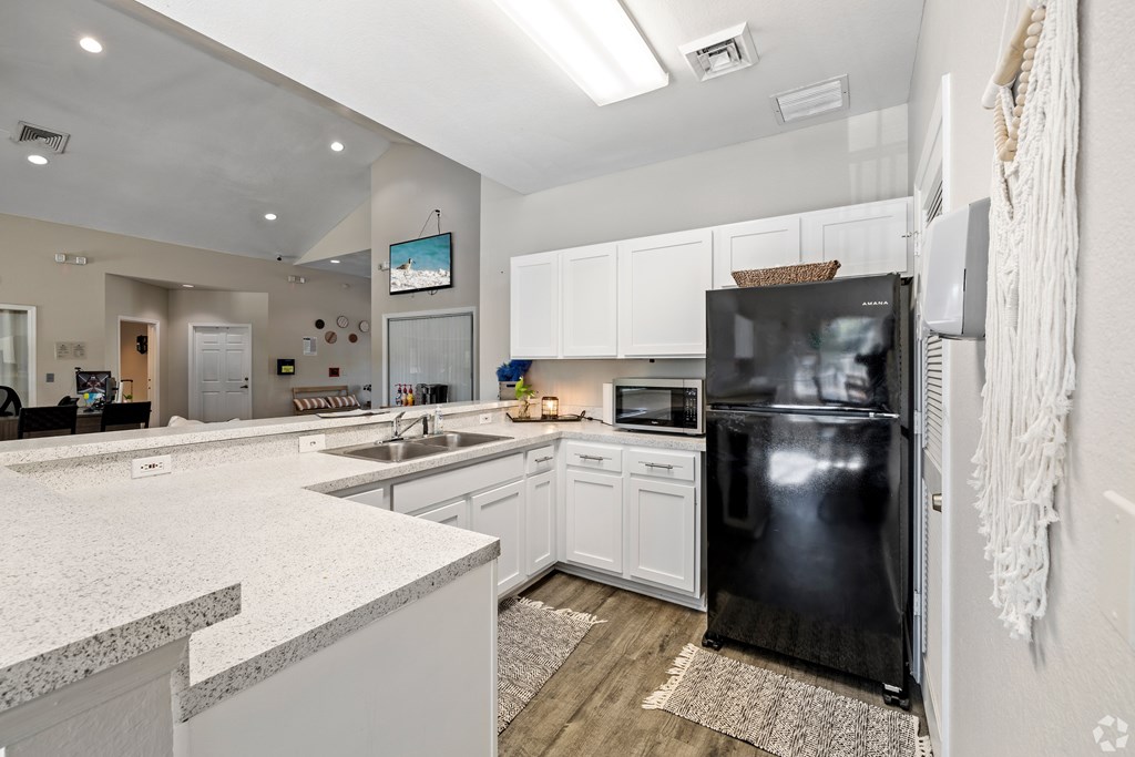 A modern kitchen with a black refrigerator and white cabinets.