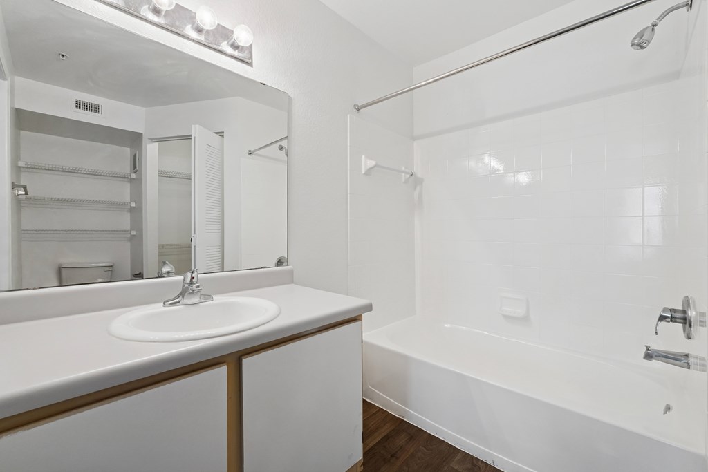 A white bathroom with a sink, mirror, and bathtub.