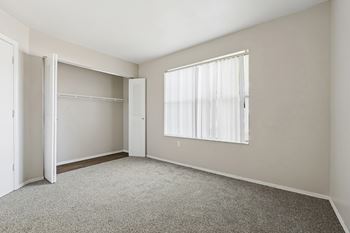 A room with a grey carpet and a window with white curtains.