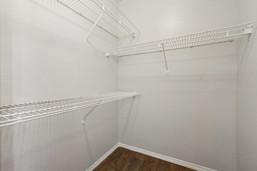 Empty white closet with shelves and a wooden floor.