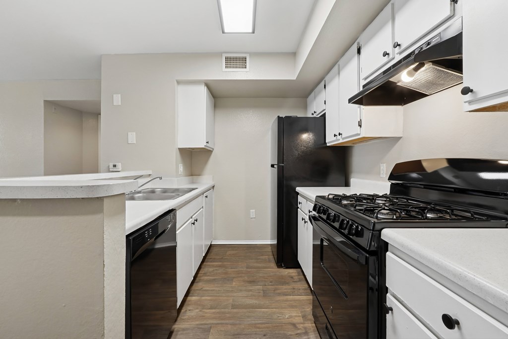 A kitchen with black and white appliances and wooden floors.