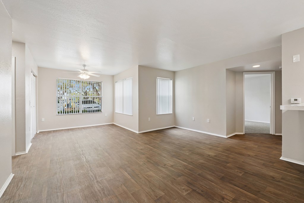 A spacious room with wooden flooring and a large window with blinds.
