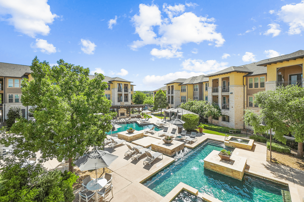a swimming pool with lounge chairs and umbrellas with apartment buildings in the background