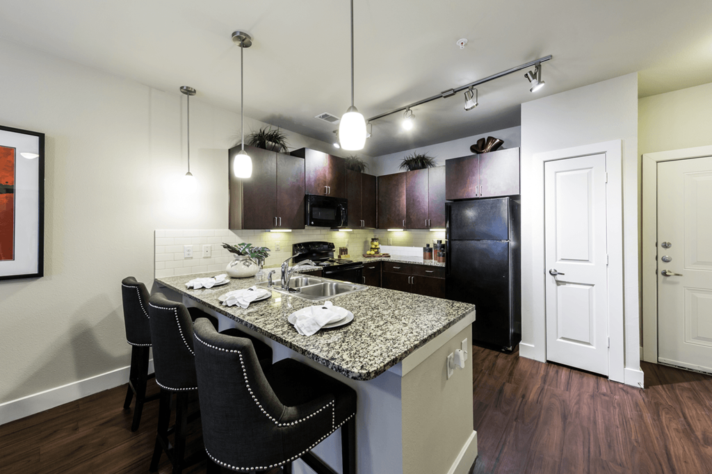 a kitchen with a large island with granite countertops and dark wood cabinets
