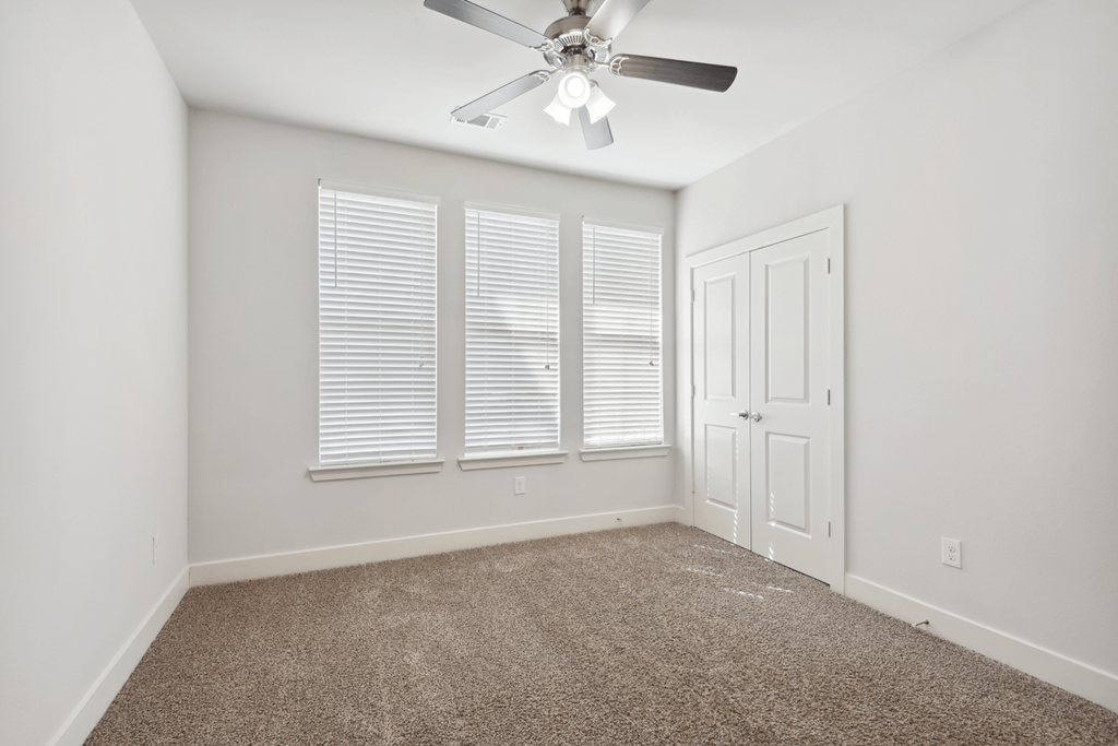 an empty room with a ceiling fan and three windows