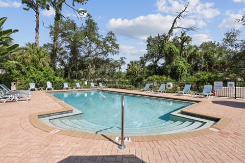 A pool surrounded by trees and chairs.