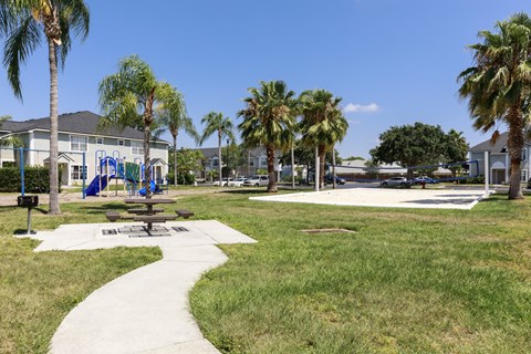Sidewalk to Picnic Table with Bench Next to Park Style Grill Between Playground and Sand Volleyball Court