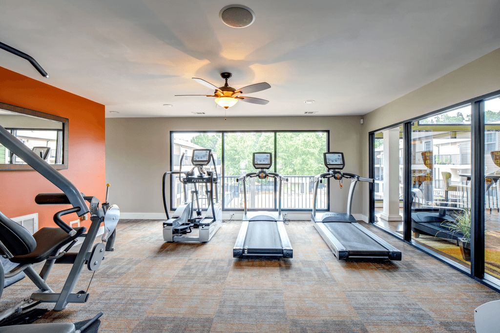 a gym with cardio machines and a ceiling fan