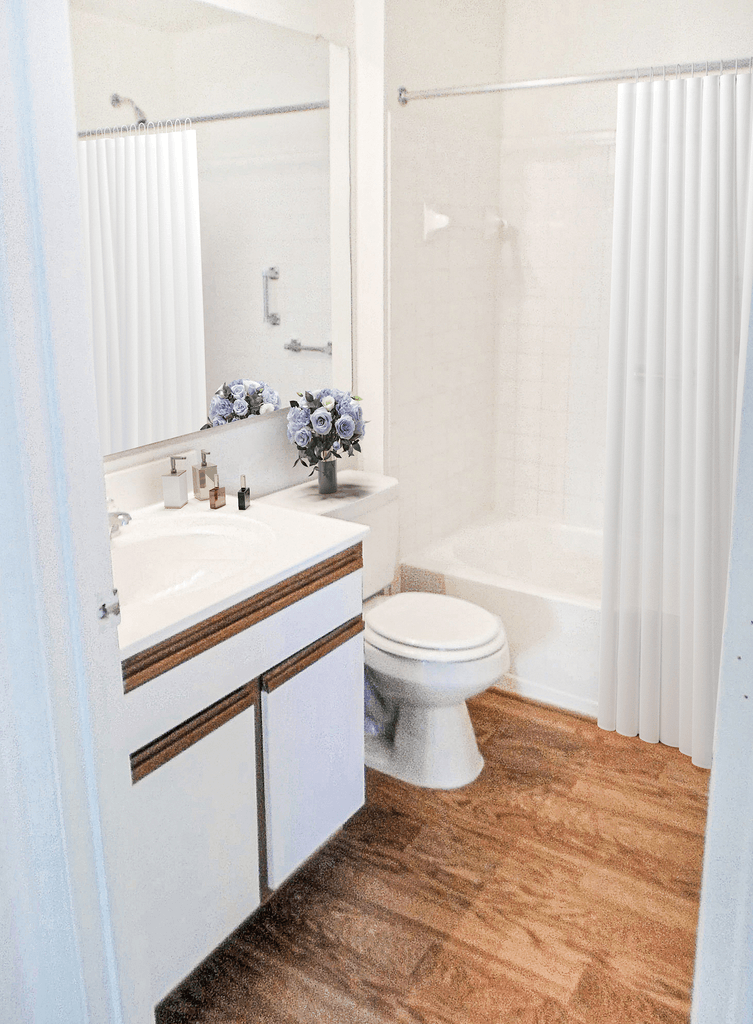 Vacant apartment bathroom with vinyl style flooring, large mirror, toilet, vanity, and a shower tub combo. Virtually staged with a shower curtain, flowers on the toilet tank, and soap on the countertop.