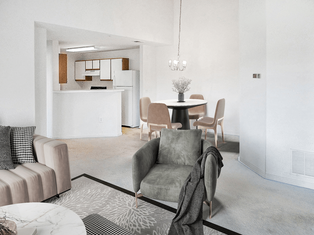 Vacant living room with tan carpet, white walls, and ceilings. The kitchen is in the background with a chandelier hanging over the dining area. Virtually staged with a couch, decorative chair, accent rug and coffee table, with dining table and four chairs in the background under the chandelier.