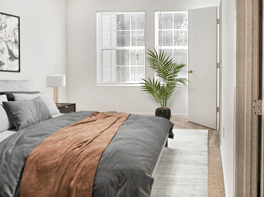Bedroom with two windows, white walls and beige carpet virtually staged with a bed, wall art, side table with lamp and a standing plant
