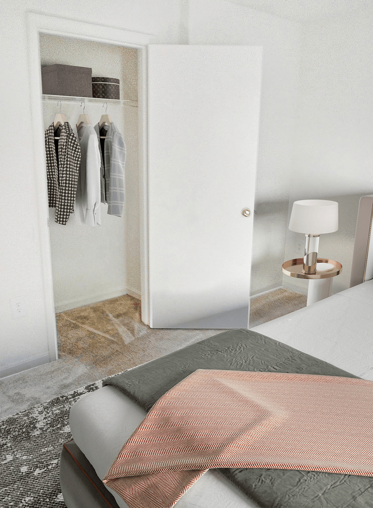 Bedroom with tan carpet, white walls, white ceilings, and a closet in the background with wired shelving virtually staged with a bed, side table with a lamp, accent rug and clothes hanging in the closet