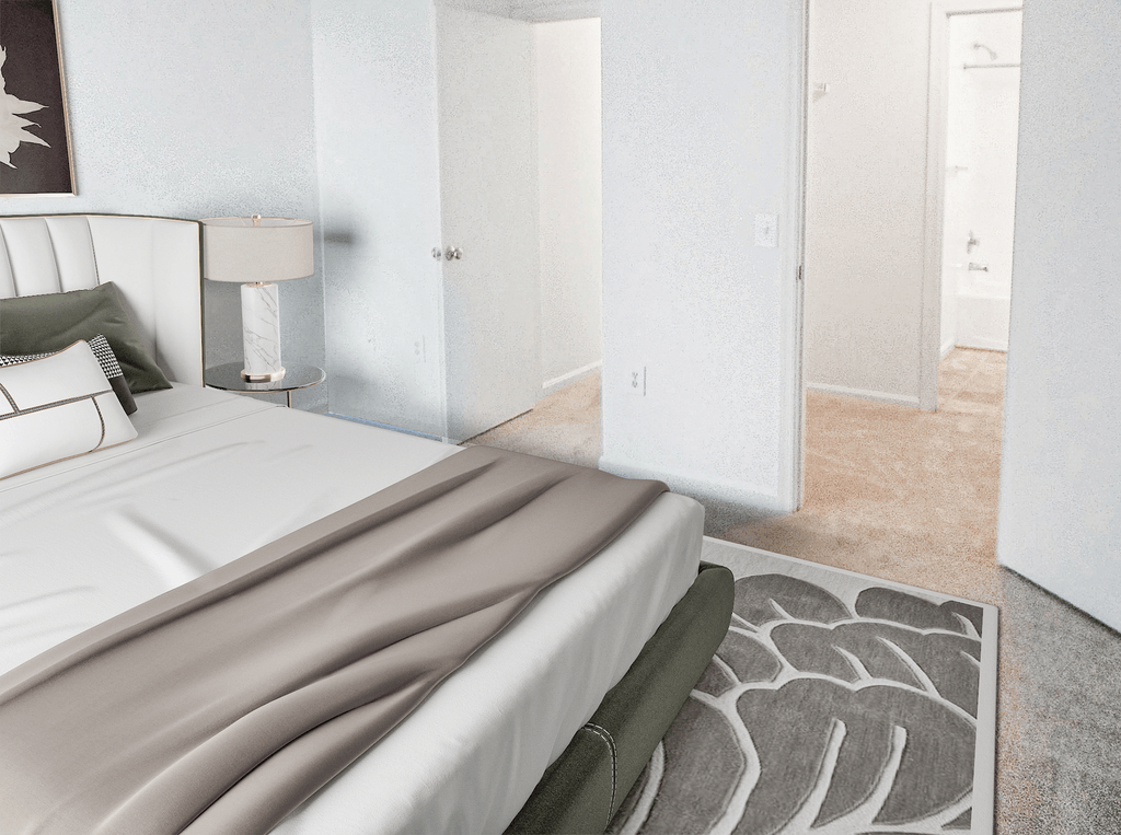 Bedroom with white walls and beige carpet virtually staged with a bed, wall art, side table with lamp and an accent rug with view of entry door and door to walk-in closet that leads to the en-suite bathroom