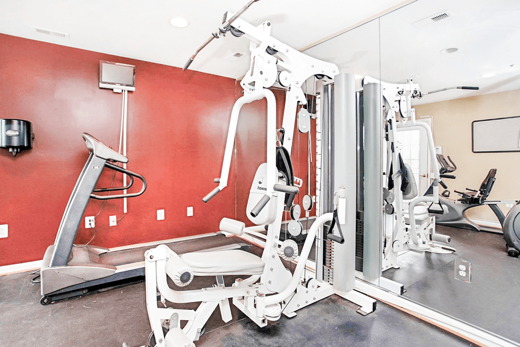 Fitness center with exercise equipment with a television on a red wall and a mirror wall behind the equipment